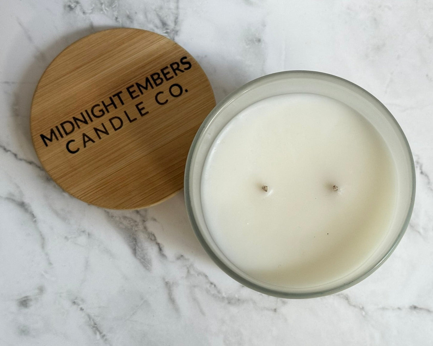 Candle with wooden lid on a marble surface, featuring 'Midnight Embers Candle Co.'