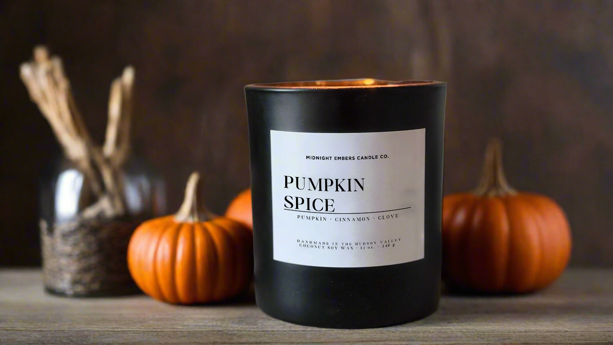 A black candle jar labeled 'Pumpkin Spice' by Midnight Smells Candle Co., styled on a wooden surface with pumpkins and a diffuser in the background.