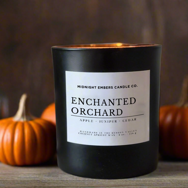 Black candle labeled 'Enchanted Orchard' with pumpkins in the background