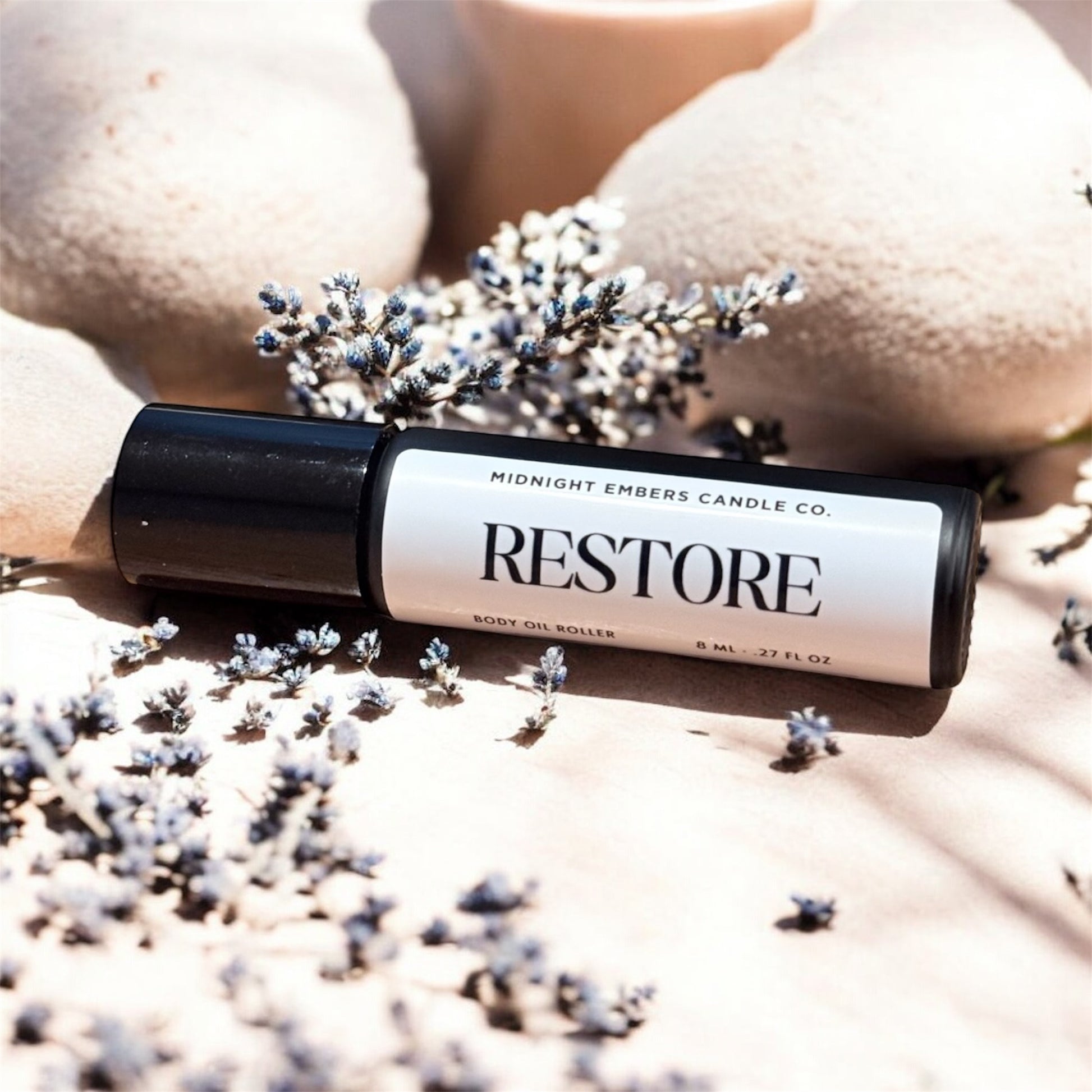 Roller bottle labeled 'Restore' from Midnight Embers Candle Co. on a textured surface with lavender flowers.