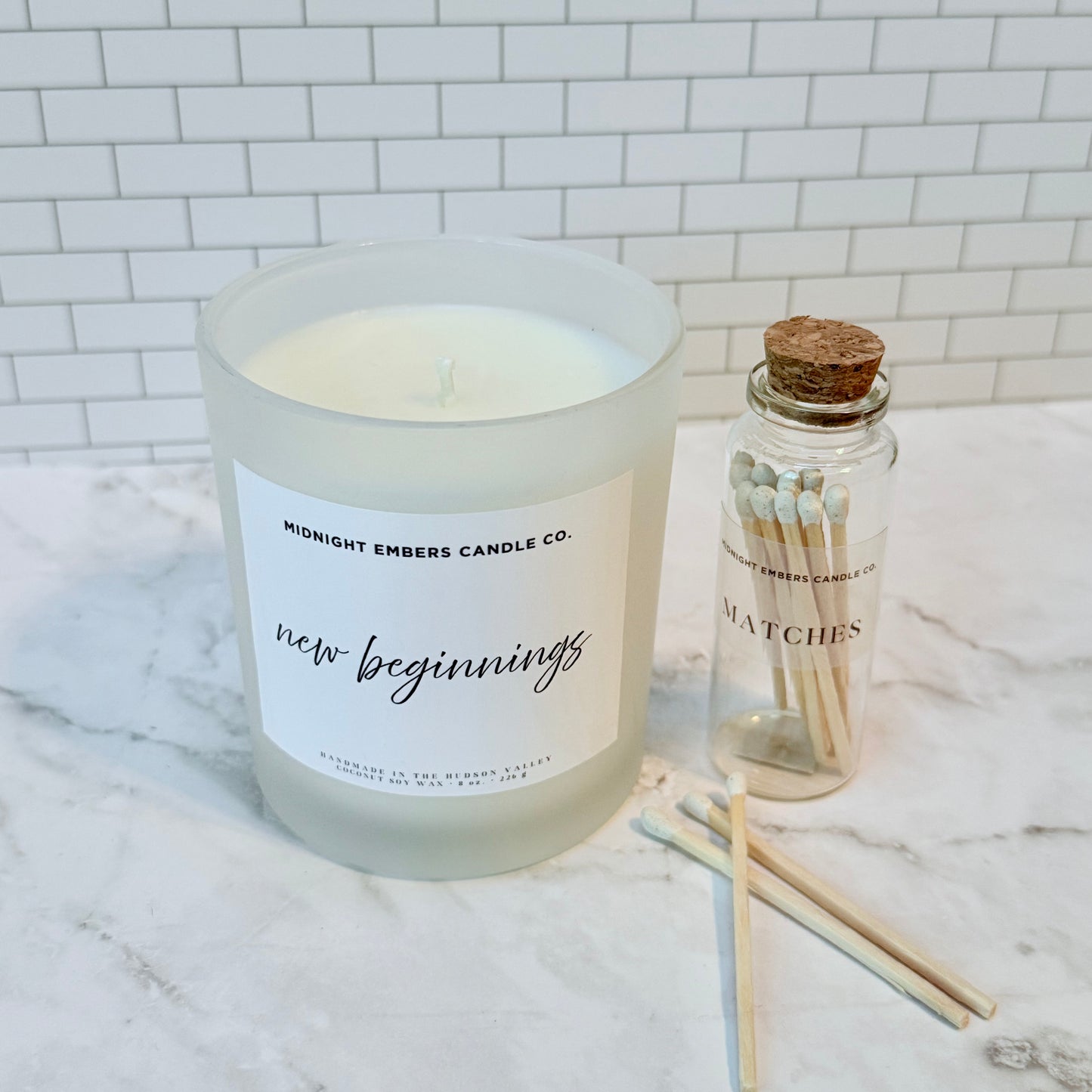 Candle with 'new beginnings' label and matches on a marble surface