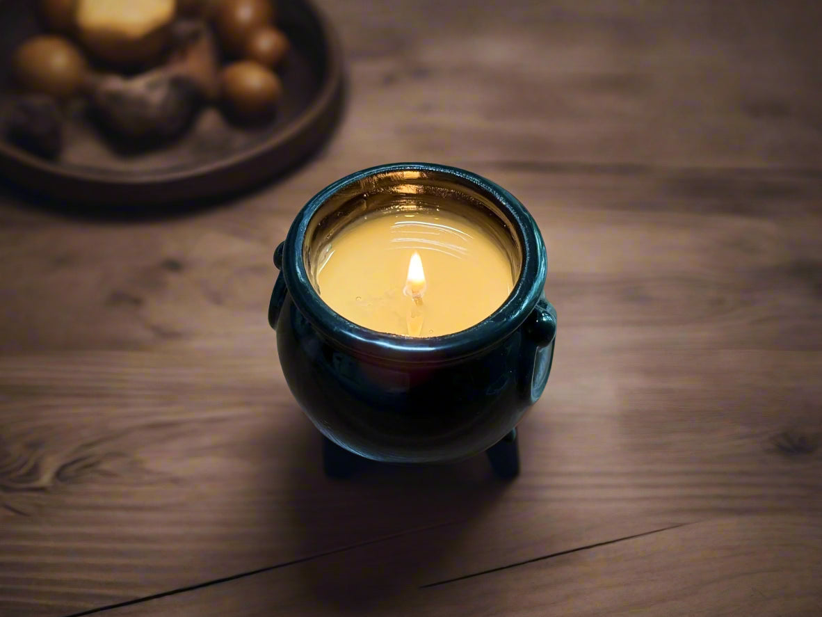 Small black ceramic container with a lit candle inside on a wooden surface