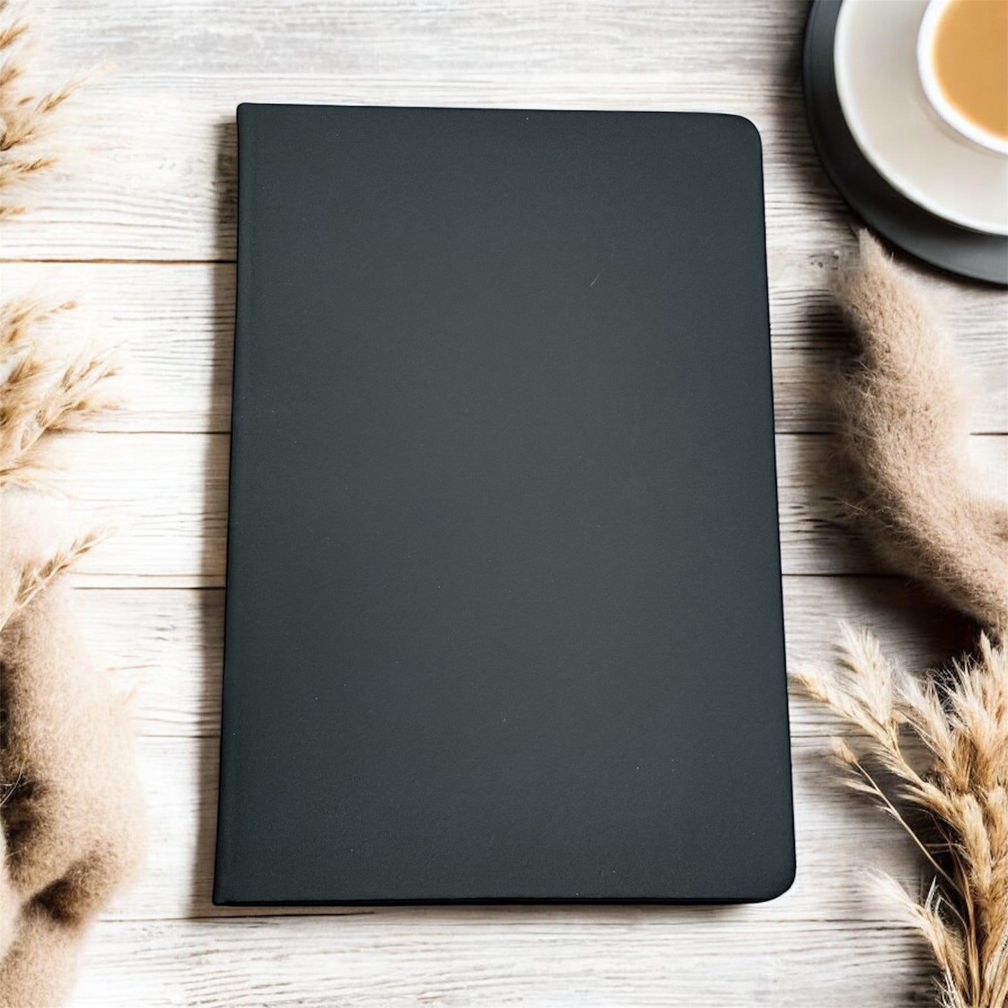 Black notebook on a wooden surface with dried plants and a cup of coffee.