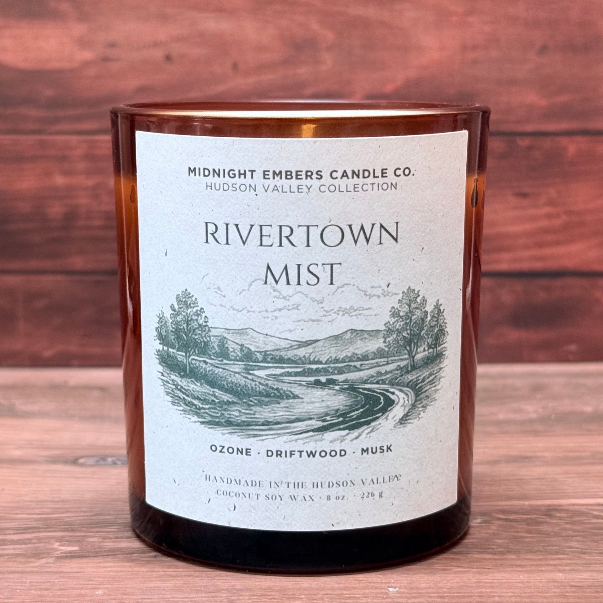 Candle labeled 'Rivertown Mist' on a wooden surface with a wooden background