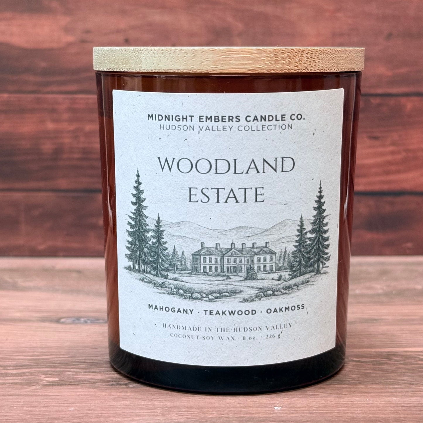 Candle labeled 'Woodland Estate' from Midnight Embers Candle Co. on a wooden surface.