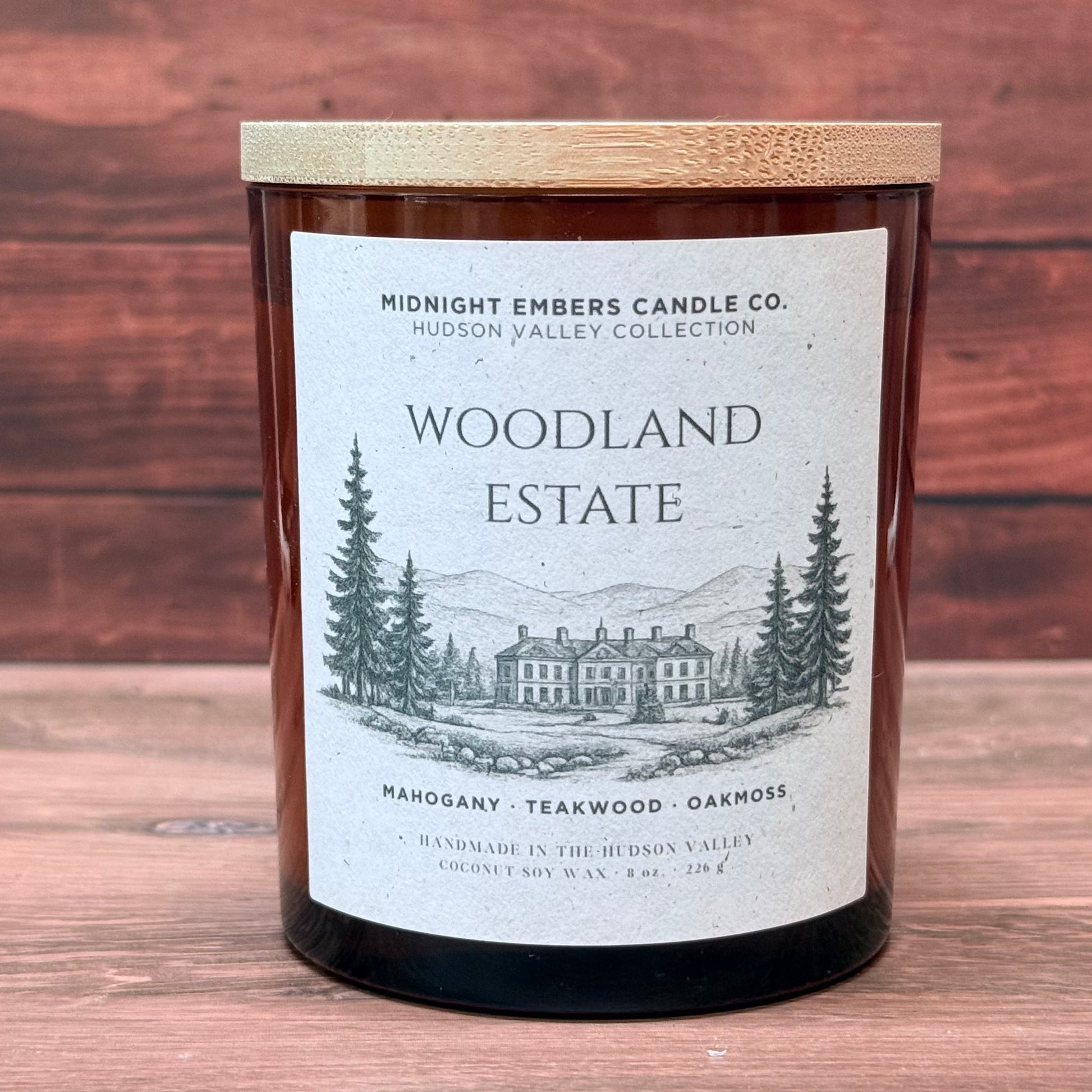 Candle labeled 'Woodland Estate' from Midnight Embers Candle Co. on a wooden surface.