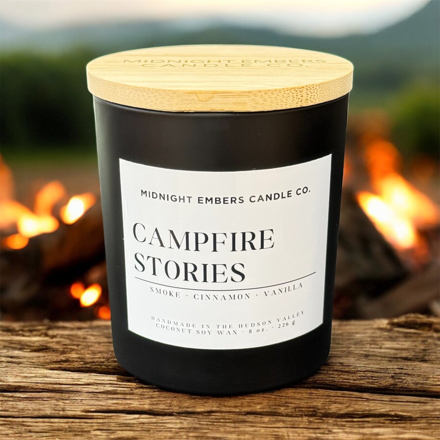 Candle labeled 'Campfire Stories' by Midnight Embers Candle Co. with a campfire in the background.