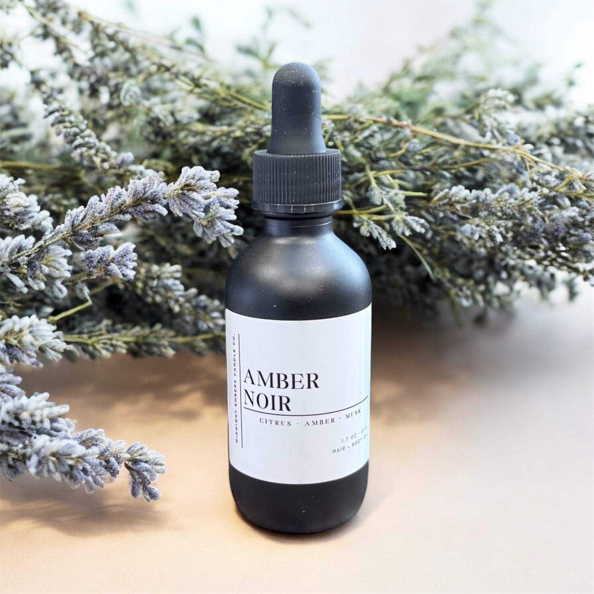 Black bottle labeled 'Amber Noir' with a dropper on a light surface with lavender in the background