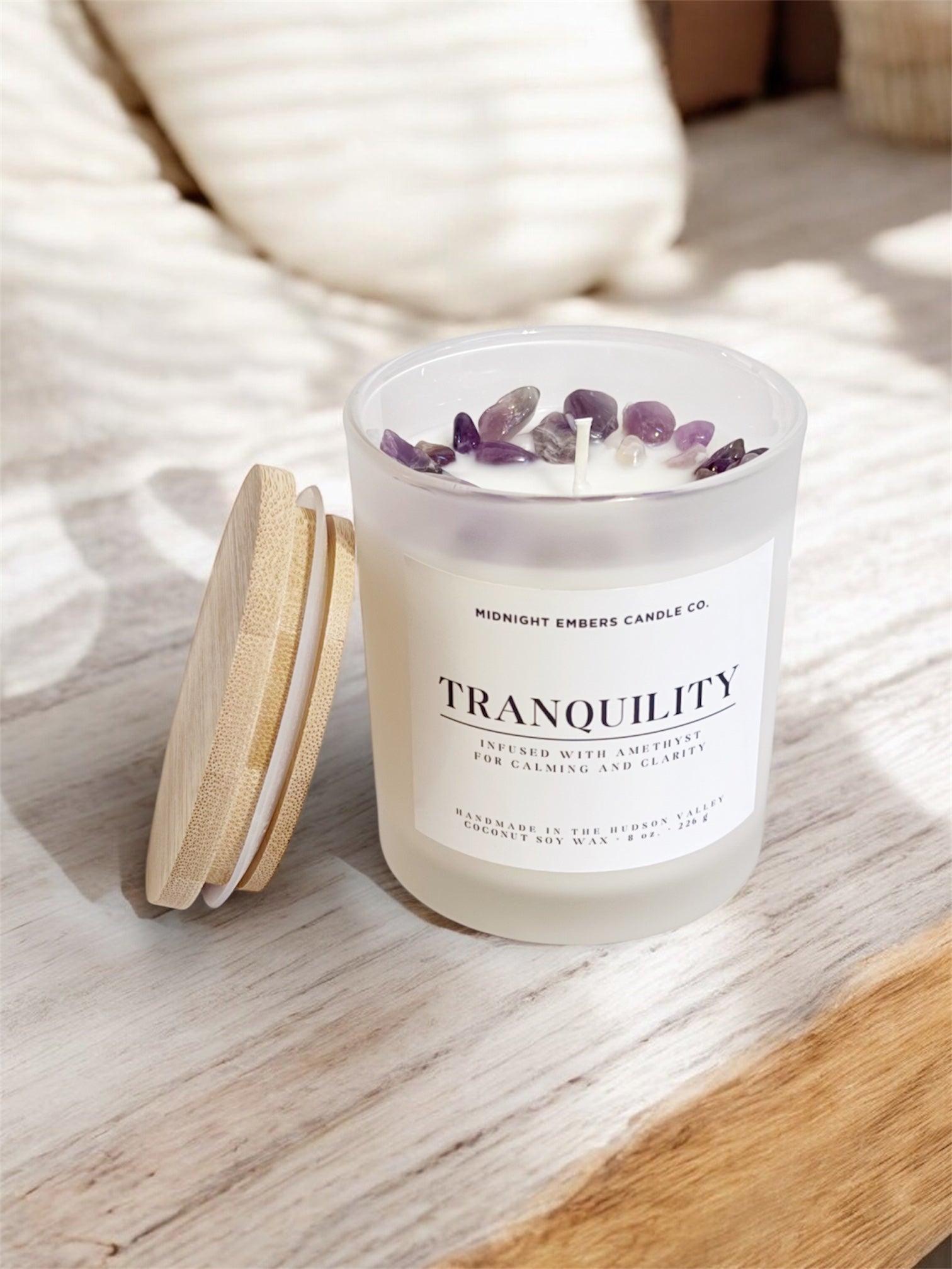Candle labeled 'Tranquility' with amethyst stones on a wooden surface