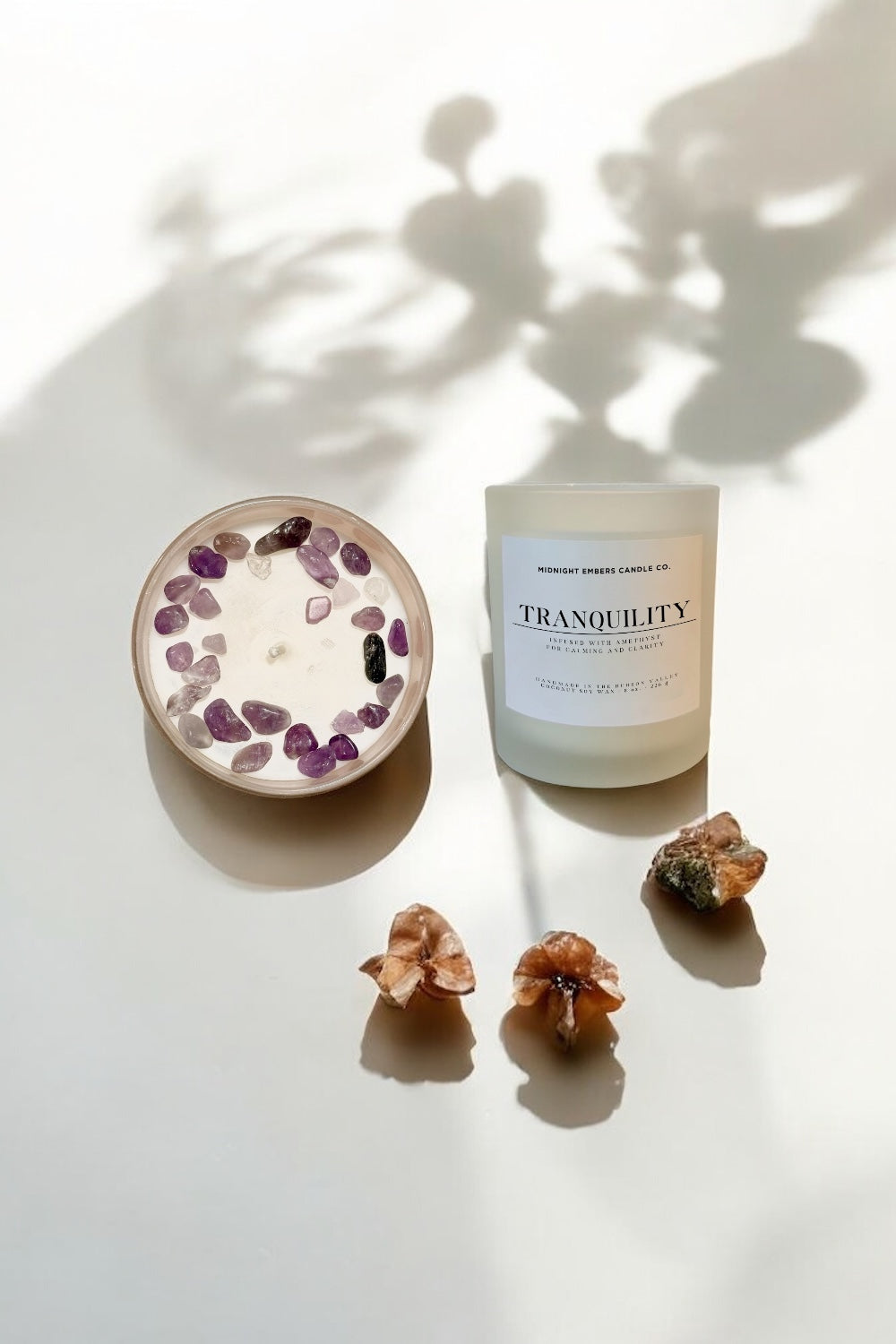 Candle labeled 'Tranquility' with decorative stones and dried flowers on a light surface.