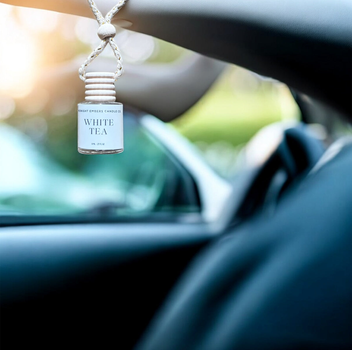 Car air freshener hanging from a car's rearview mirror with 'White Tea' fragrance.