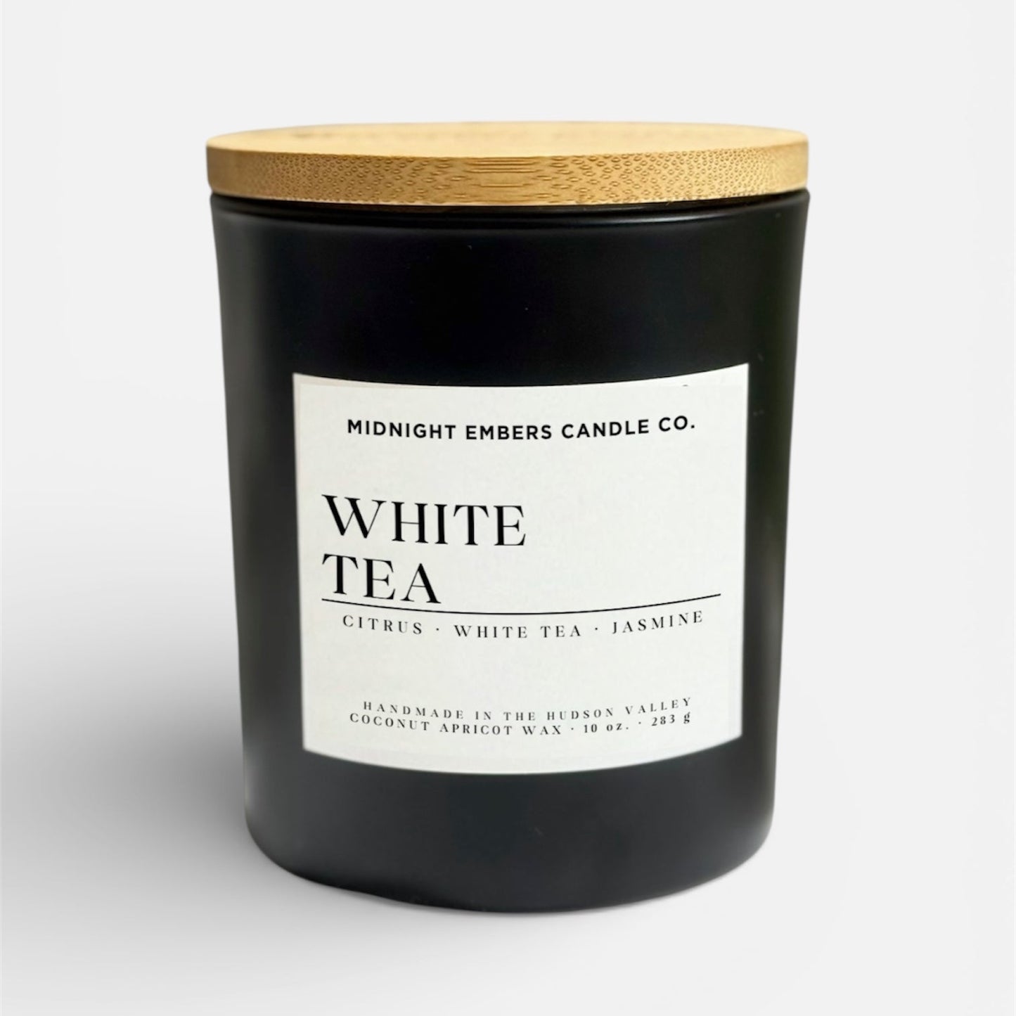 Black candle with a wooden lid labeled 'White Tea' from Midnight Embers Candle Co.